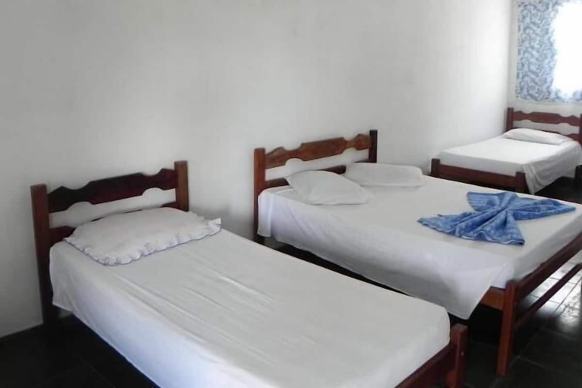 Une chambre avec trois lits simples, chacun doté d’une tête de lit en bois et de draps blancs.