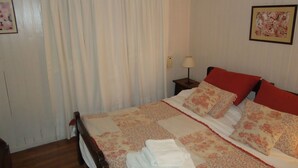 Uma cama bem arrumada com roupa de cama florida, uma cabeceira de madeira e uma mesinha de cabeceira com abajur.