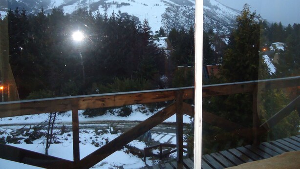 Vista de uma varanda com guarda-corpo de madeira, com vista para uma montanha coberta de neve e uma área arborizada.