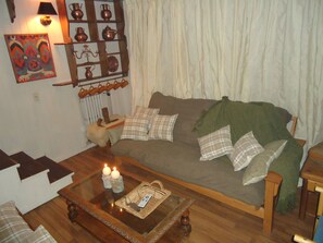 Una sala de estar acogedora con un sofá marrón, cojines de cuadros, una mesa de centro de vidrio con velas y una estantería con cerámica.