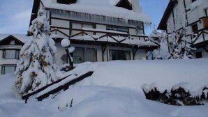 Um edifício coberto de neve com estilo arquitetônico tradicional, destacando um telhado inclinado e vigas de madeira.