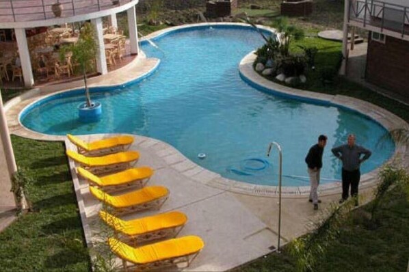 Une piscine avec des chaises longues jaunes et un espace de détente abrité.