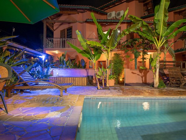 A poolside area with a stone floor, lounge chairs, and a bar area with a pool.