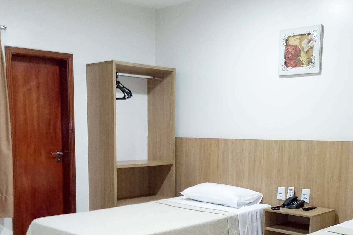 Une chambre d’hôtel avec deux lits, une armoire en bois, un petit bureau avec un téléphone et une œuvre d’art accrochée au mur.