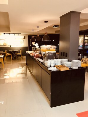 Un área de desayuno de hotel moderna con una barra central, asientos y una máquina de café.
