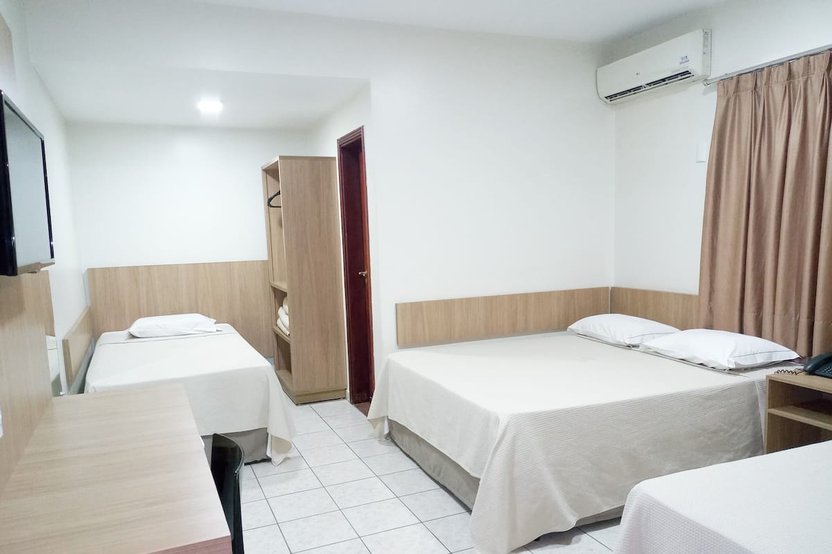Une chambre d’hôtel avec deux lits simples, une armoire en bois, un bureau et un appareil de climatisation.