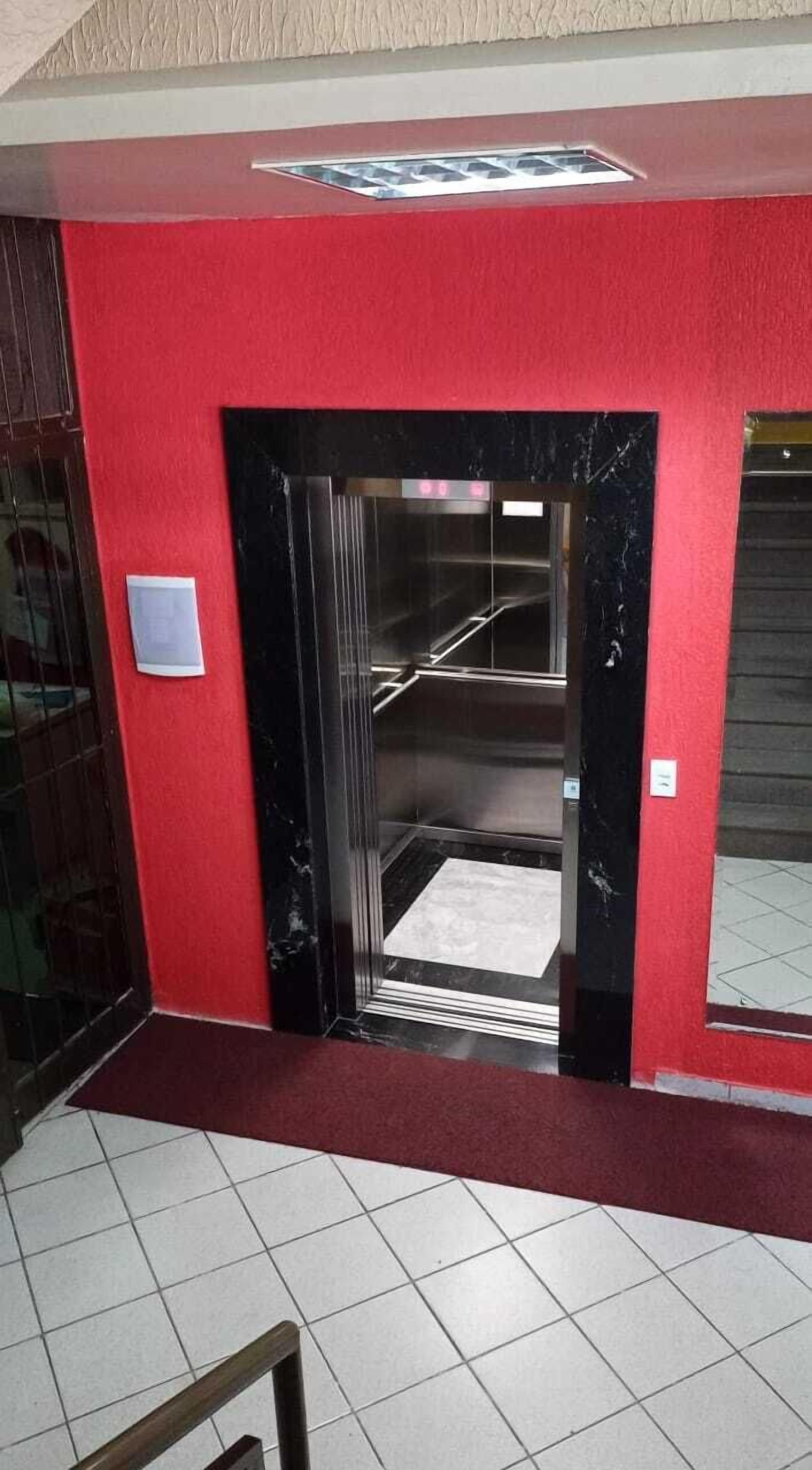 A red wall with a black elevator door and a tiled floor.