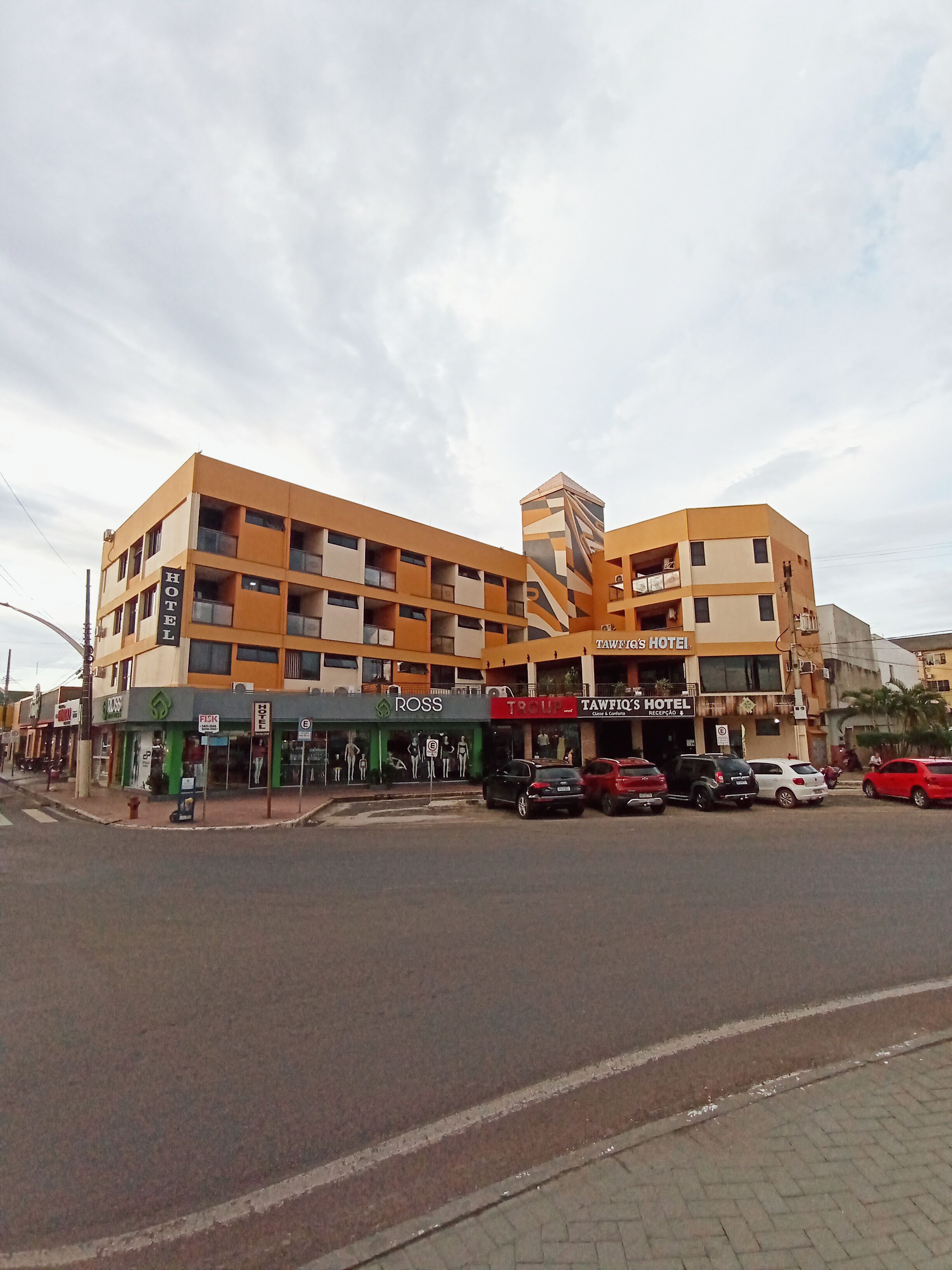A multi-story hotel with balconies, a central tower, and several ground-level shops.
