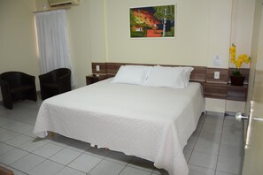 A hotel room with a bed, two chairs, a nightstand, a painting, and a potted plant. - Hotel O Compadre (Porto Velho)