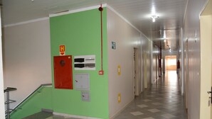 A hallway with green walls, a red emergency exit sign, and a fire alarm. - Hotel O Compadre (Porto Velho)