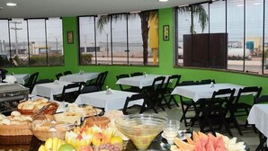 A buffet setup with various fruits and bread in a room with green walls and large windows. - Hotel O Compadre (Porto Velho)