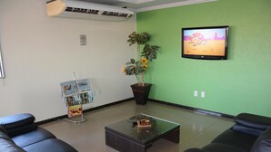 A reception area with a green wall, a flat-screen TV, a coffee table, and black leather sofas. - Hotel O Compadre (Porto Velho)