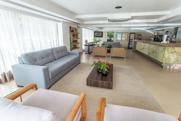 Ein großzügiger Wohnbereich mit grauem Sofa, einem Couchtisch aus Holz mit Pflanzen und einem Empfangsbereich mit Marmorplatte.