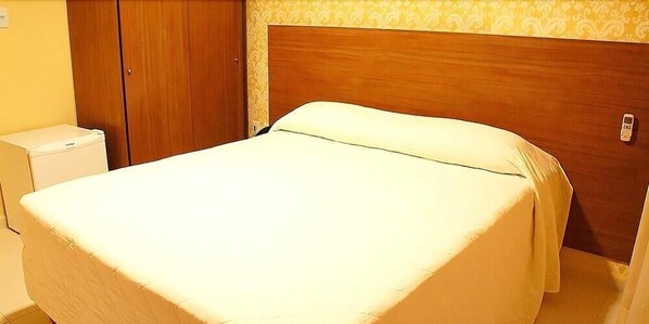 Una cama individual con cabecera de madera, una mesita de noche pequeña y un armario.