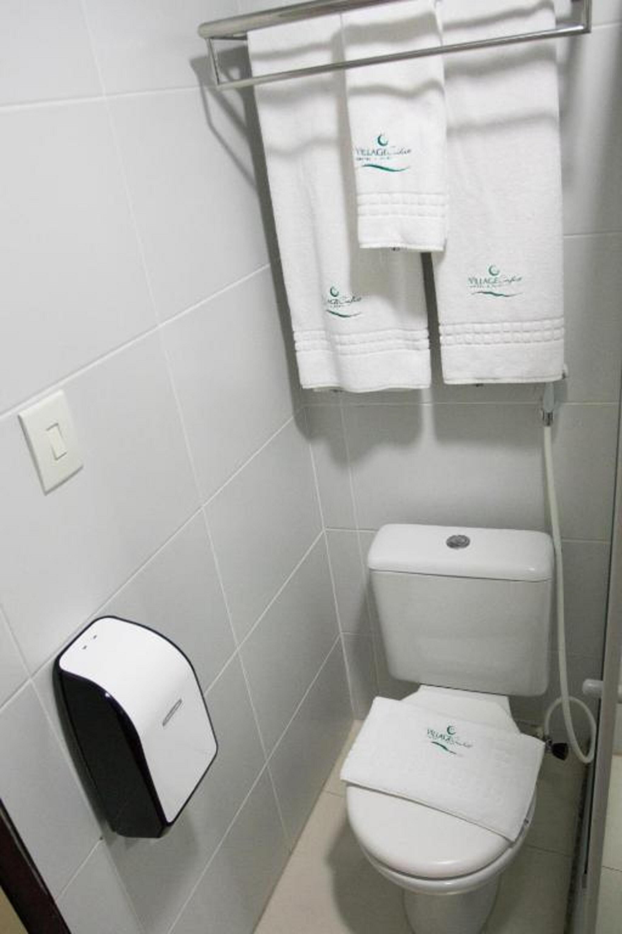 Une salle de bain équipée de toilettes, d’un sèche-mains et de deux serviettes suspendues à un porte-serviettes.