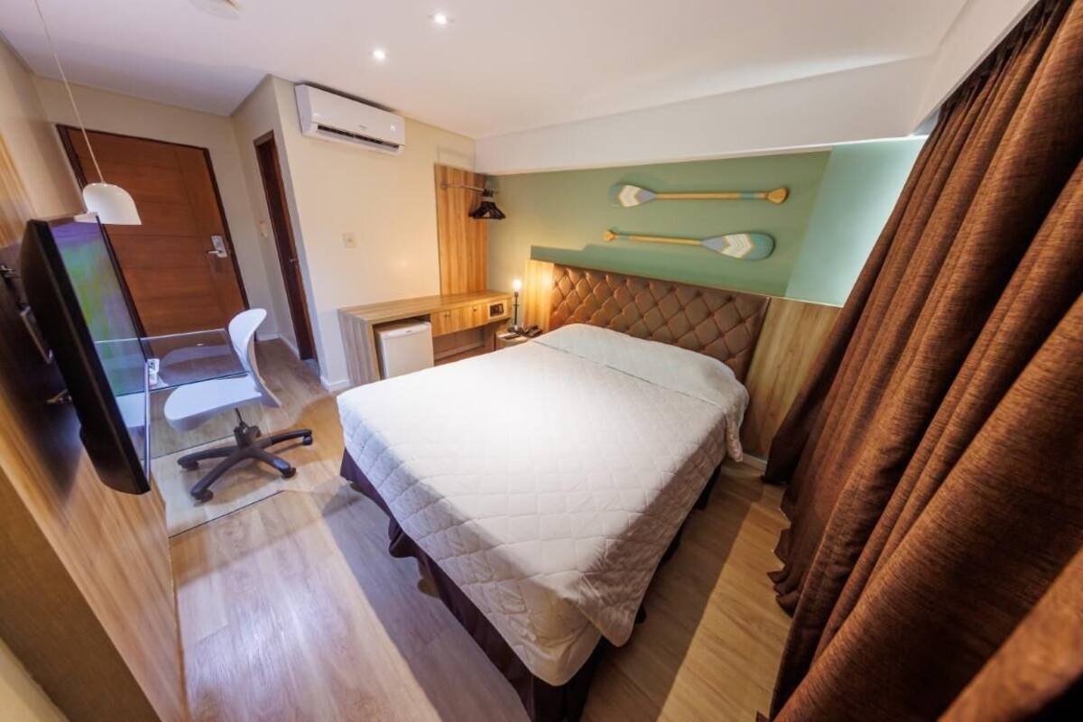 Une chambre d’hôtel équipée d’un lit, d’un bureau, d’une chaise, d’un climatiseur et d’un téléviseur fixé au mur.