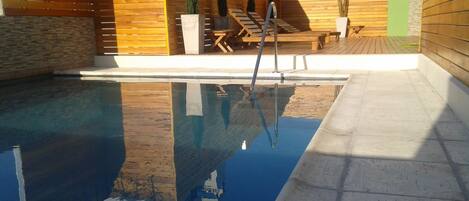 Una piscina con cubierta de madera y sillones de descanso.