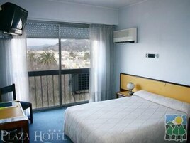 Habitación de hotel con cama, ventana con vistas, una silla, una mesa y un aire acondicionado.