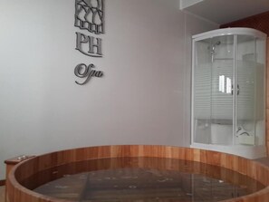 A spa area with a wooden tub, a glass-enclosed shower, and a wall with a PH spa logo.
