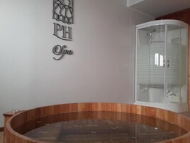 Un área de spa con una bañera de madera, ducha con cerramiento de vidrio y una pared con el logotipo de PH spa.