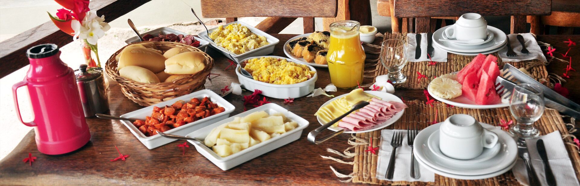 A breakfast buffet with various dishes, a red water bottle, and dining utensils on a wooden table.