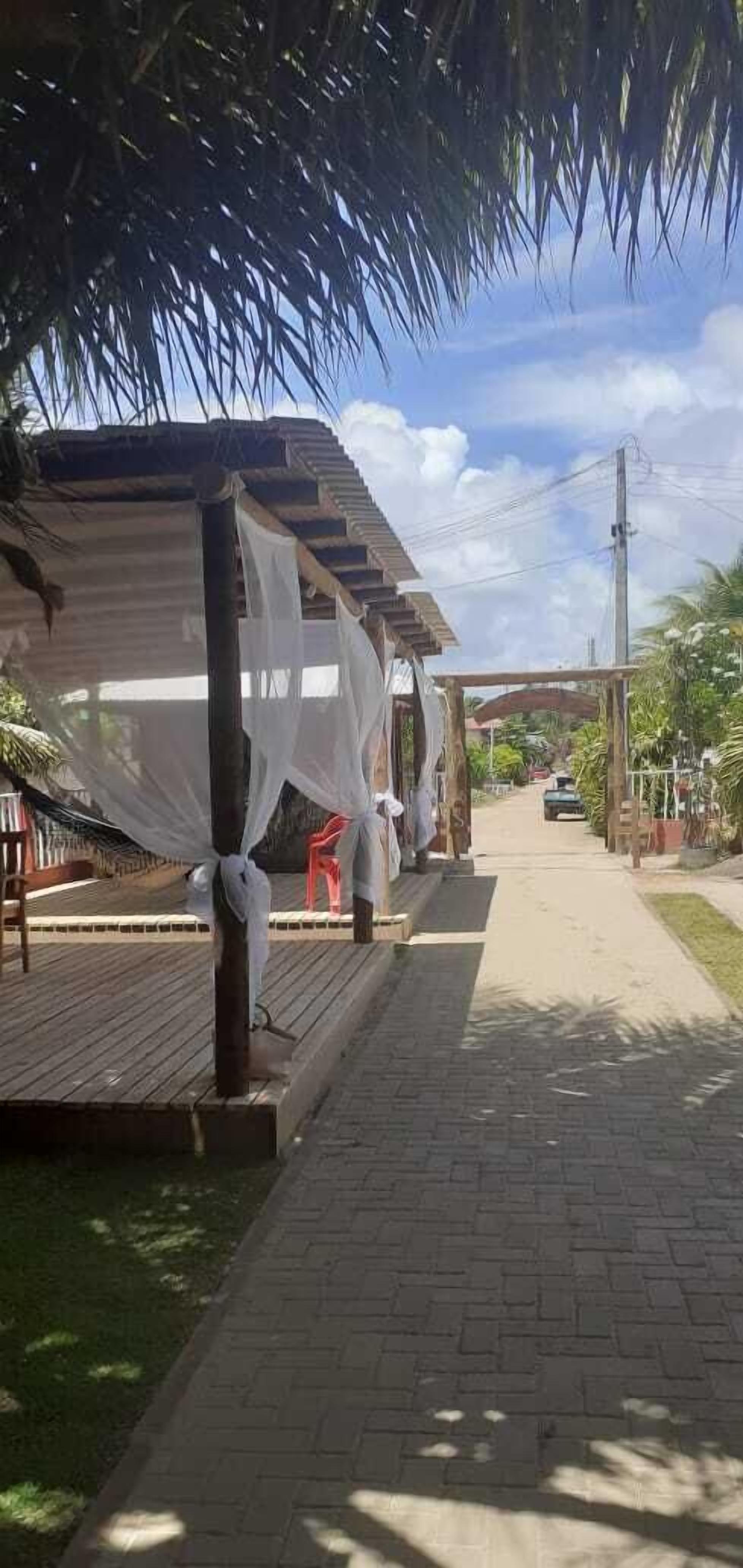 Uma galeria coberta com deck de madeira, palmeiras e céu aberto.