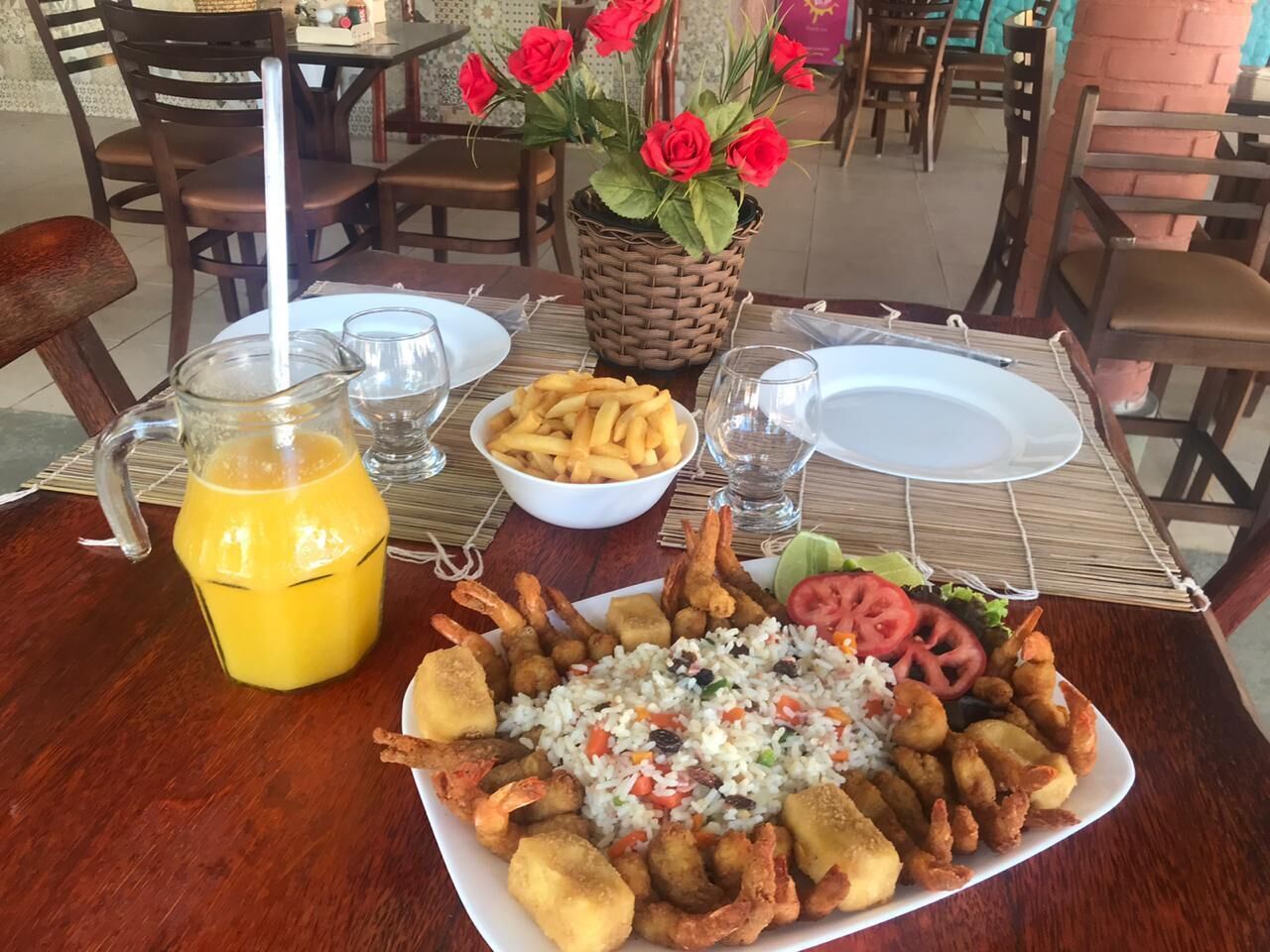 Una mesa de comedor con un plato de mariscos fritos, una jarra de jugo de naranja y una cesta de rosas rojas.