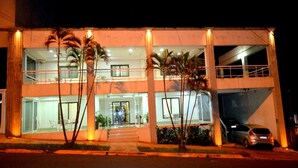 Un edificio de dos pisos con fachada de vidrio, palmeras frente a él y un coche estacionado afuera.