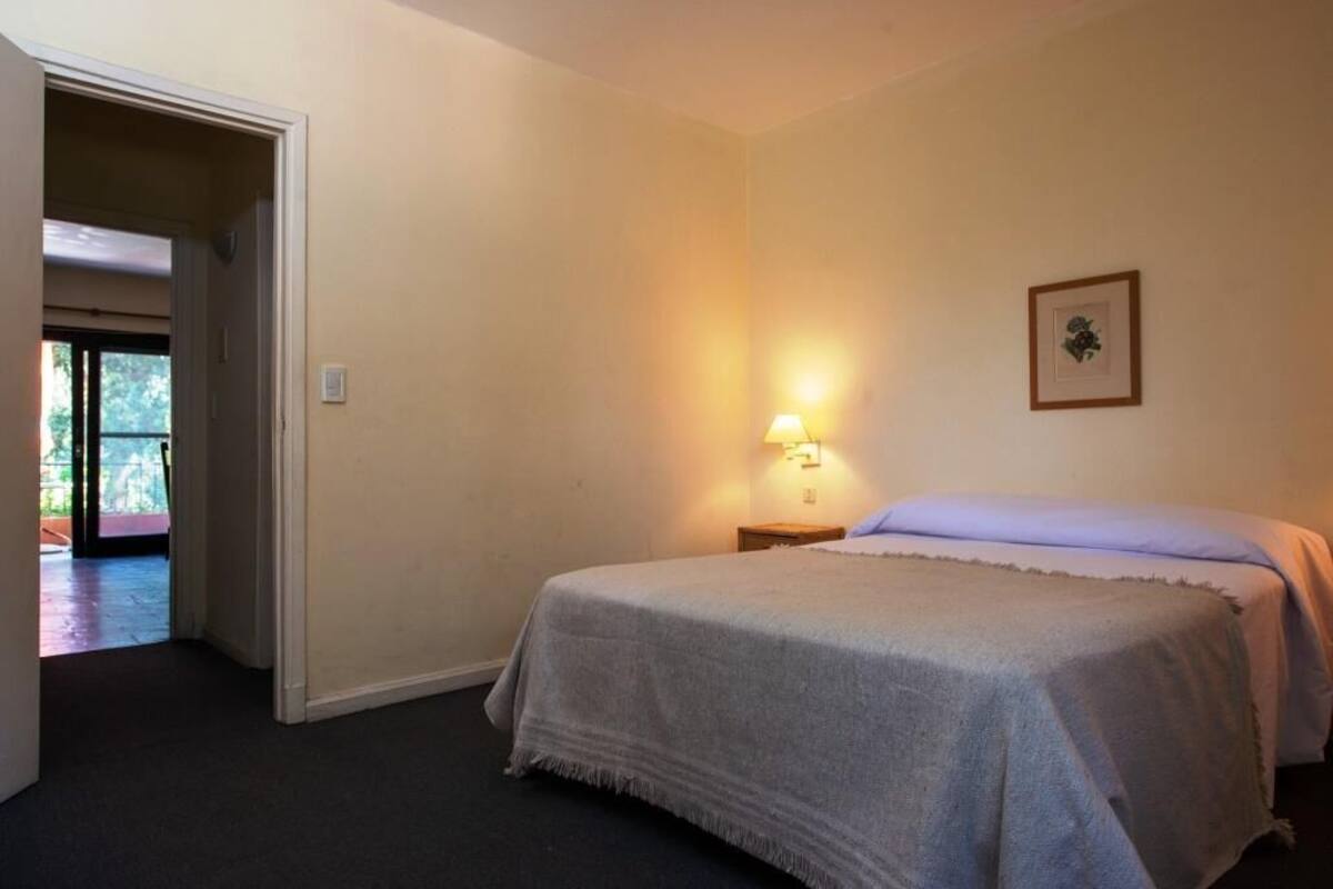 A bedroom with a bed, a nightstand, a wall-mounted lamp, and a framed picture.