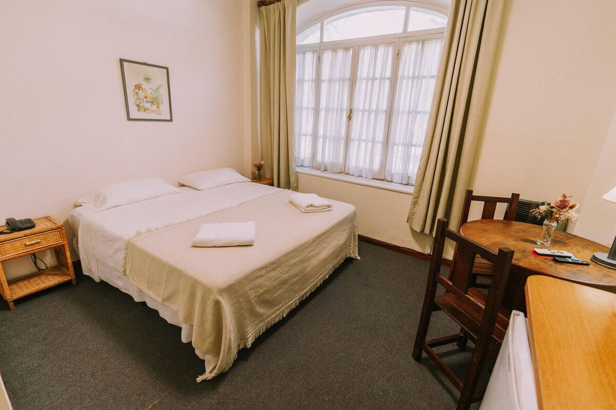 A neatly arranged hotel room with a bed, bedside table, and a small table with chairs.