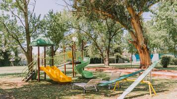 Explore the park's playground, featuring a green slide, yellow slide, climbing structure, and climbing net, surrounded by trees and grass.