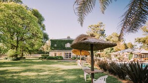 A lush garden with a pool, outdoor seating, and a building with a green roof. - Hotel Apartur Mar del Plata (Mar del Plata)