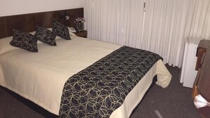 A hotel room with a large bed, a wooden headboard, a bedside table with a vase of flowers, and a window with white curtains. - Hotel Morales (San Clemente)