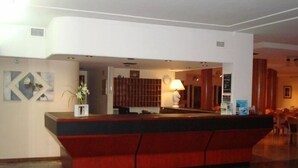 A reception area with a wooden reception desk, a potted plant, and a wall clock. - Hotel Morales (San Clemente)