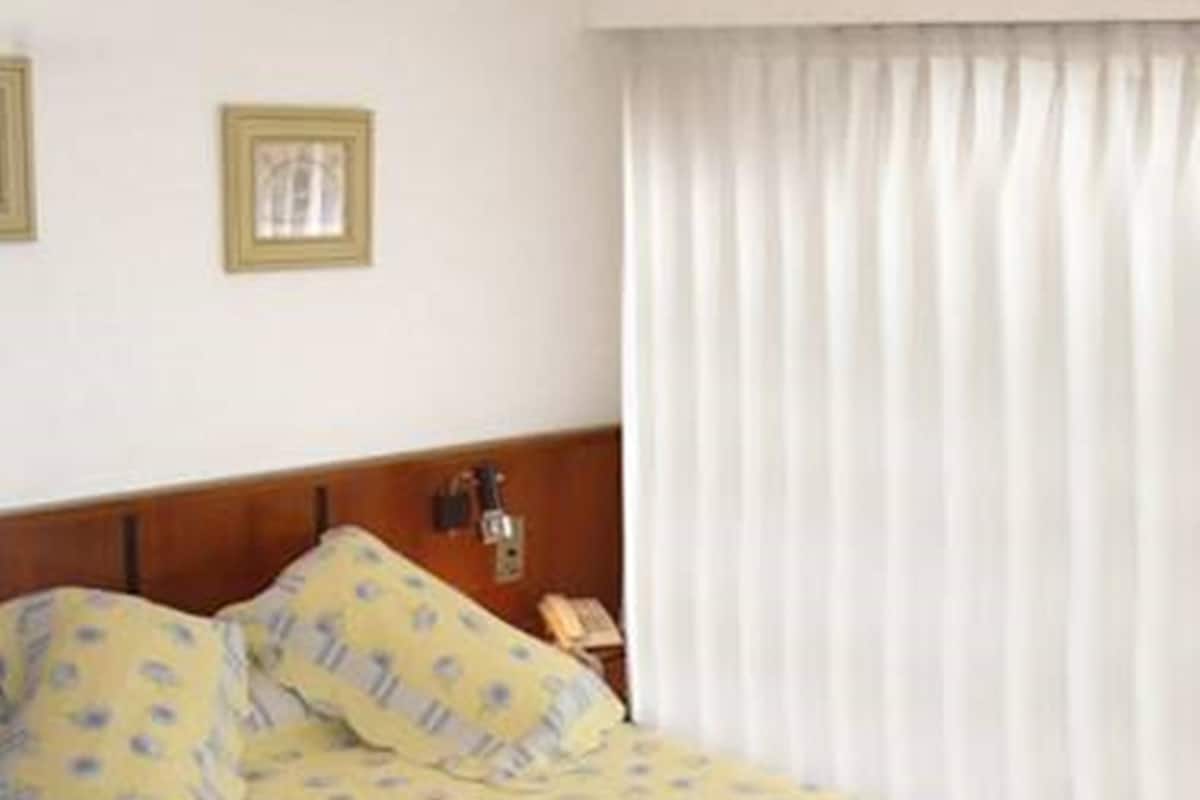 Ein Hotelzimmer mit Bett, Nachttisch, Lampe und einem Fenster mit Vorhängen.