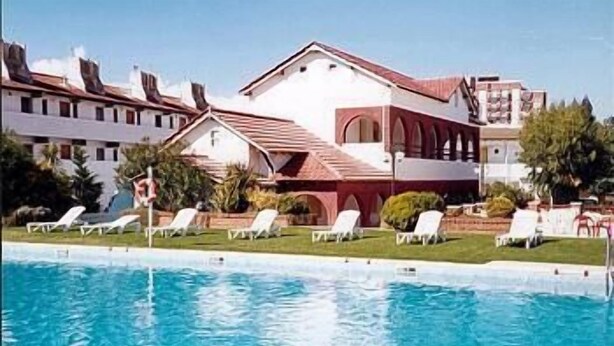 A swimming pool with lounge chairs and a building with a red roof and white walls. - Hotel Morales (San Clemente)