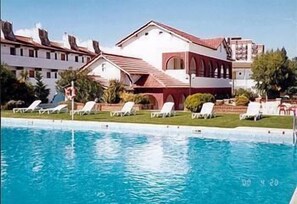 En swimmingpool med liggestole og en bygning med rødt tag og hvide vægge.