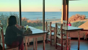 A room with a large window overlooking the sea, wooden furniture, and a table with items on it.