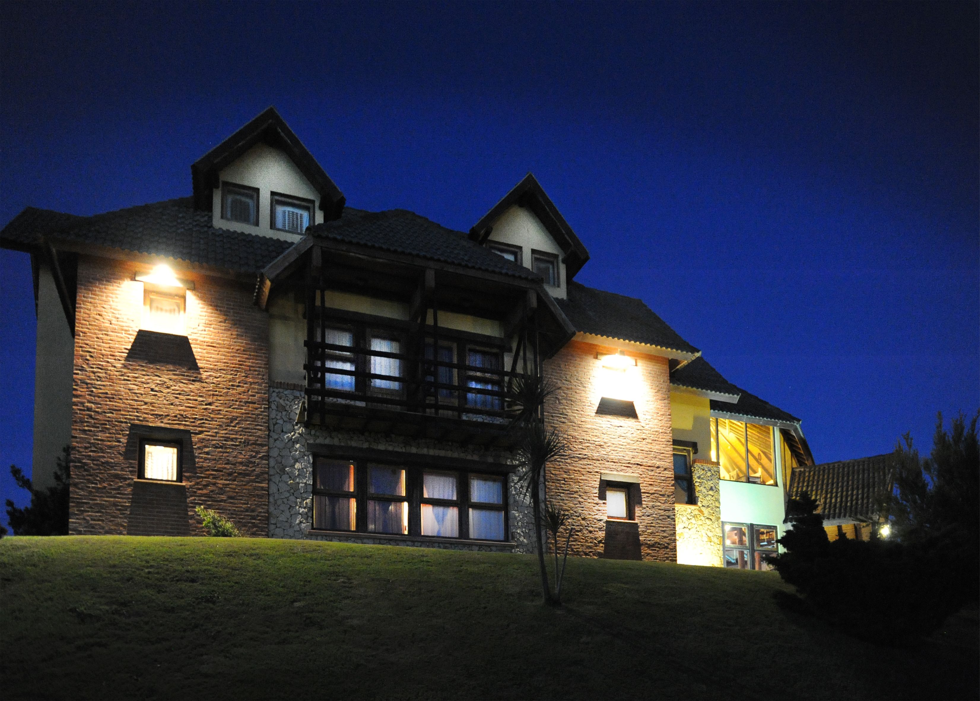 A large, multi-story house with a stone facade, multiple windows, and a well-lit exterior at night.