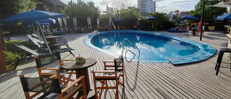 A wooden deck with a pool, lounge chairs, and umbrellas.