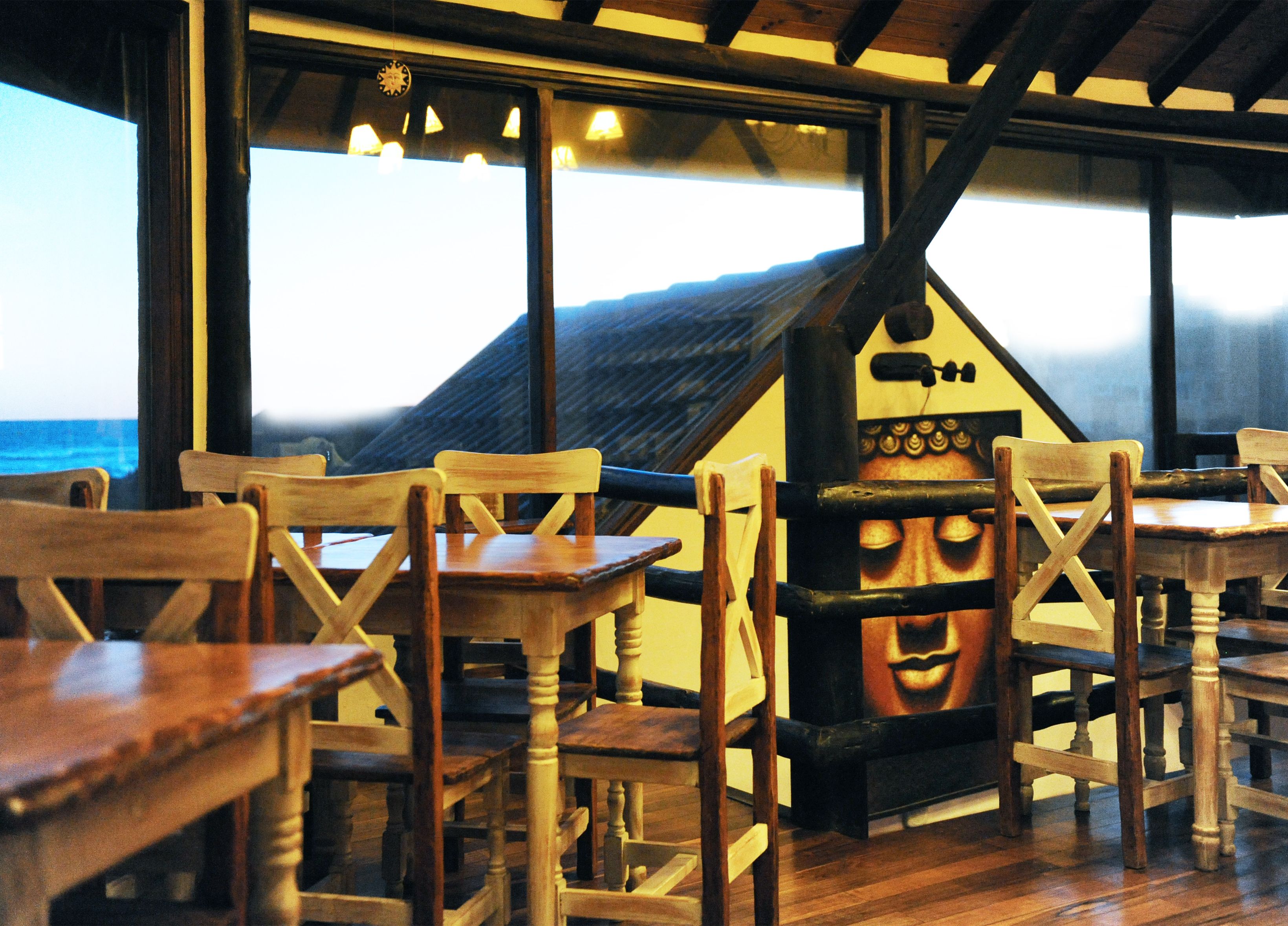 A restaurant interior with wooden tables and chairs, a large window overlooking a building, and a mural on the wall.