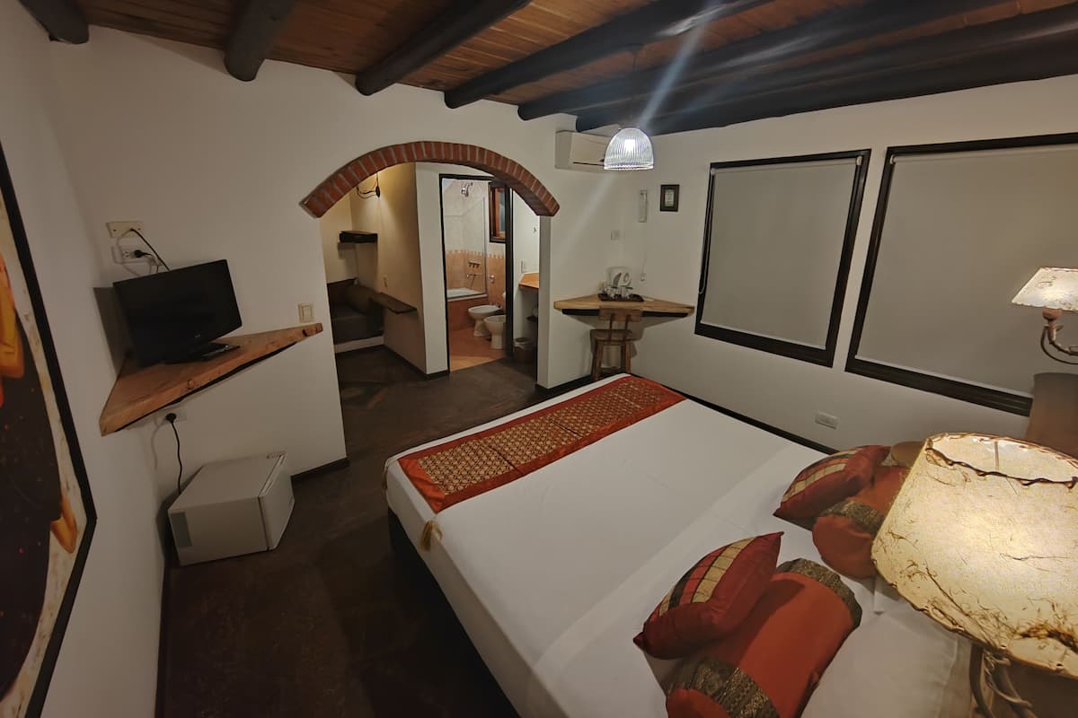 A bedroom with a bed, a TV, a desk, and a bathroom visible through an archway.