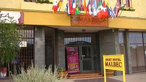Een hotelingang met meerdere vlaggen, een bordje waarop 'APART HOTEL MALBEC' staat en een bord 'SALÓN MALBEC'.