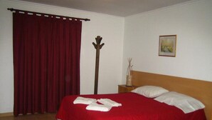 Een slaapkamer met een groot bed, een houten hoofdbord, een nachtkastje met een vaas en een rood gordijn.