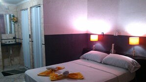A hotel room with a bed, two bedside lamps, a nightstand, a bathroom with a sink, and a shower. - Posada La Alemana (Puerto Iguazu)