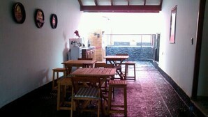 A dining area with wooden tables and chairs, a small kitchen area, and a view of the outside. - Posada La Alemana (Puerto Iguazu)