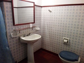 Casa de banho com lavatório branco, espelho, sanita e azulejos estampados.