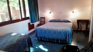 A room with two beds, a chair, a small table, and a window with curtains. - Hosteria La Cabaña (Puerto Iguazú)