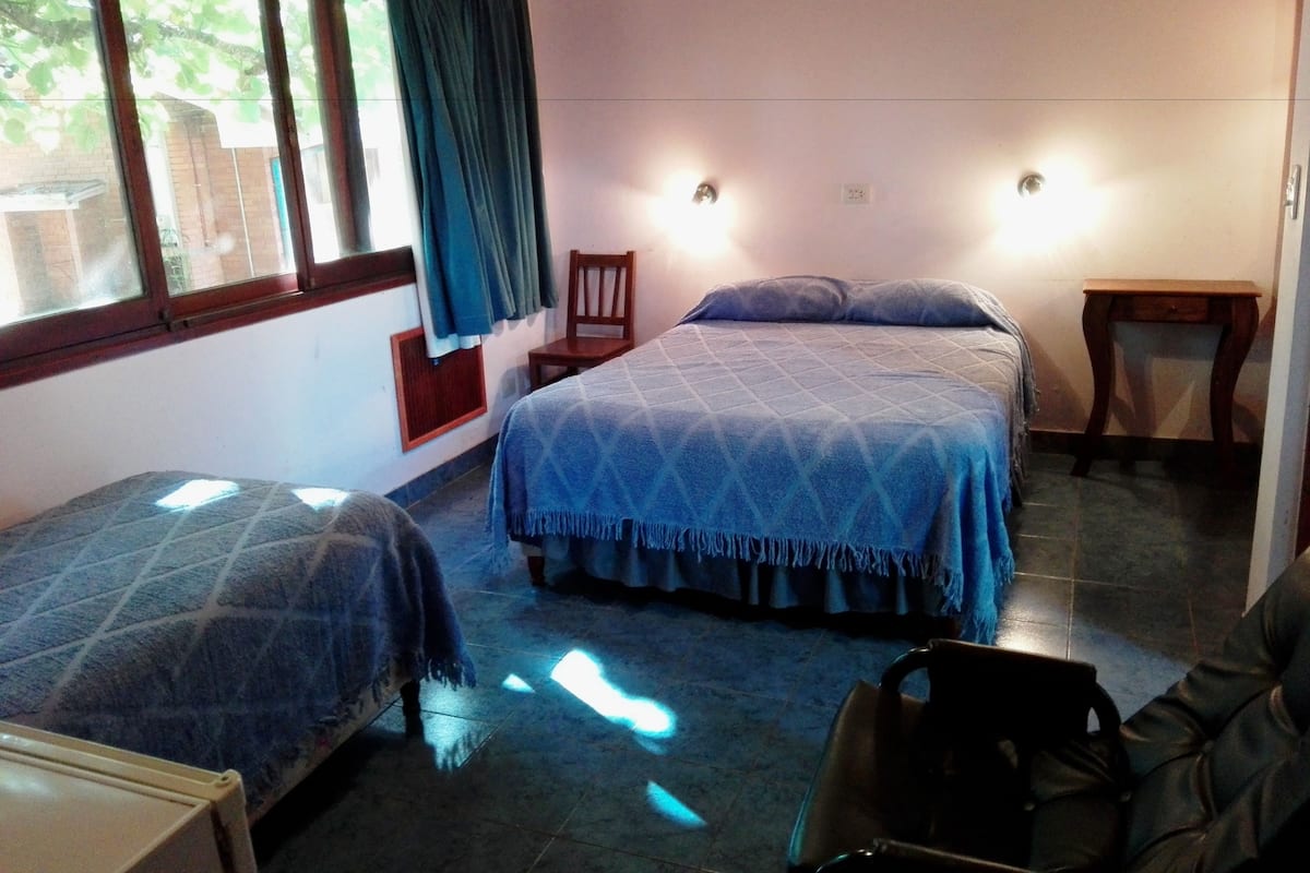 A room with two beds, a chair, a small table, and a window with curtains.