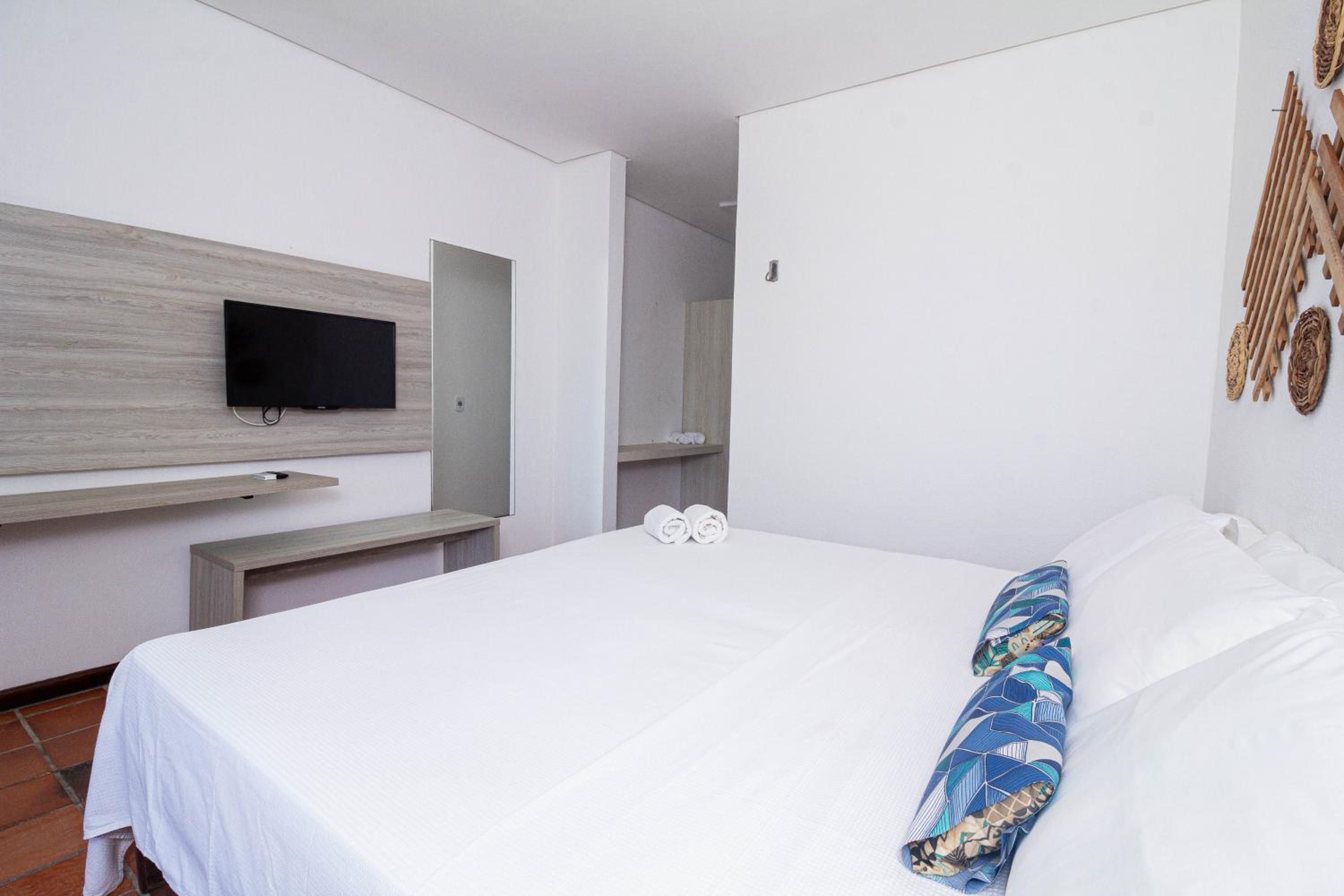 Quarto de hotel com cama, televisão de tela plana na parede e prateleira de madeira.